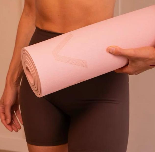 Een vrouw houdt een roze Bloom Yogamat van Cabau vast